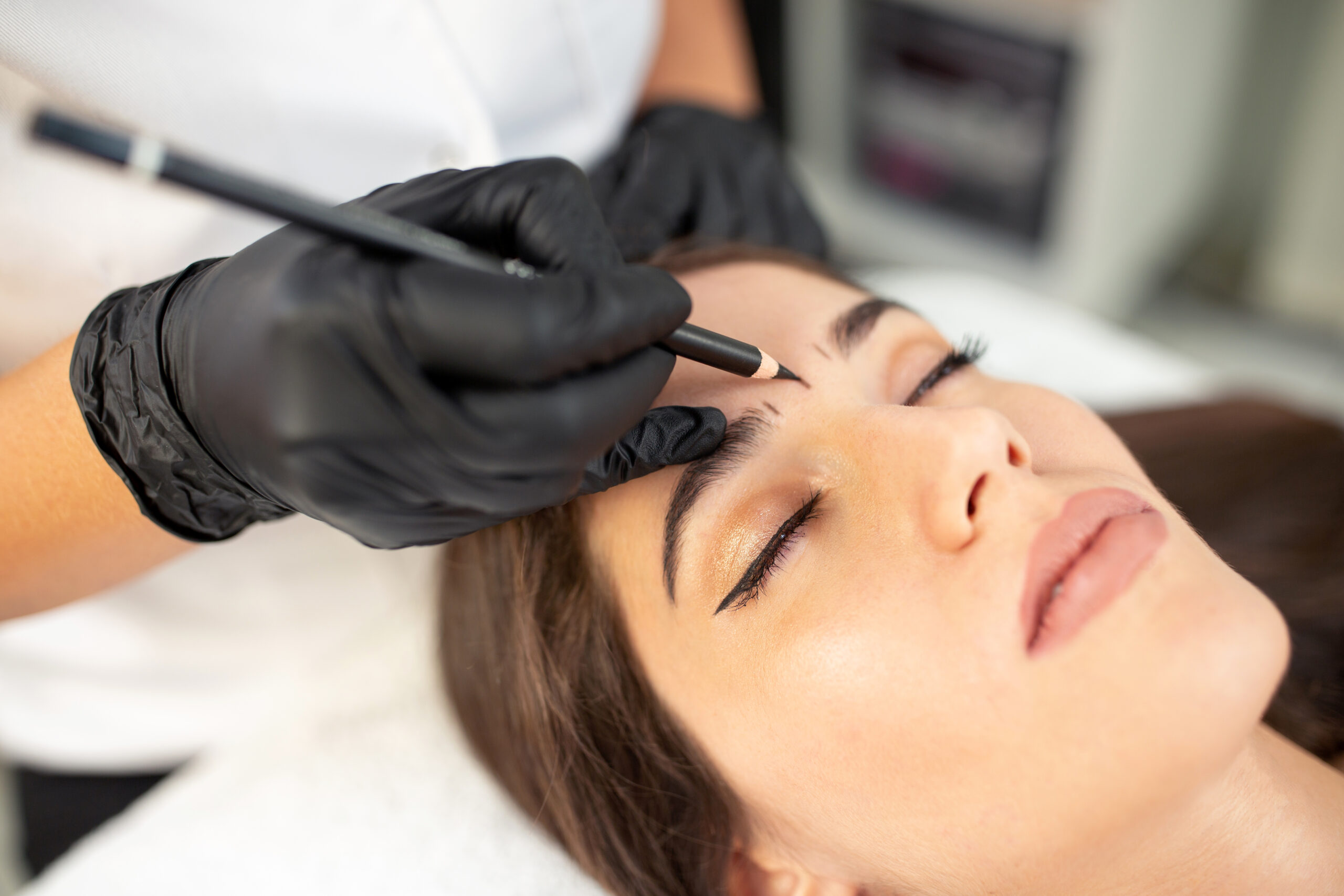 Certified beautician preparing her client eyebrows in order to apply more precise and hair-like strokes